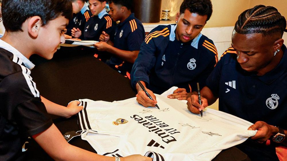 Vinícius y Rodrygo firmando una camiseta del Real Madrid y a un aficionadO.